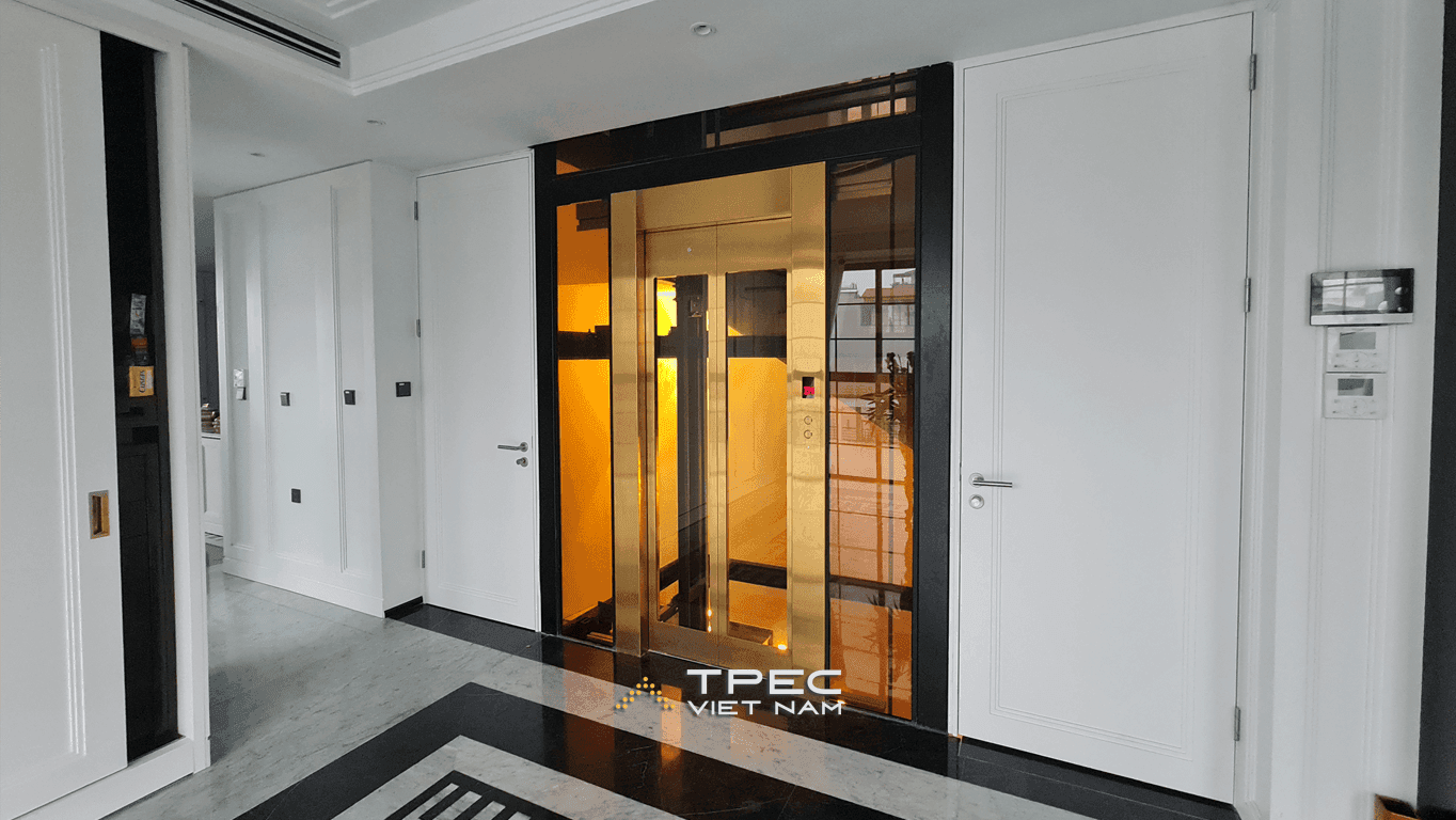 Thang máy kính cửa inox vàng, giếng khung đen giữa sảnh căn hộ phố Tôn Đức Thắng