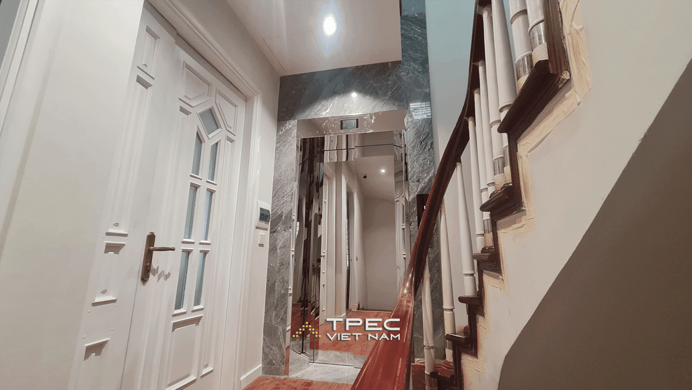 Thang máy gia đình cửa inox gương ốp đá marble xám bên cầu thang nhà Nguyễn Khang