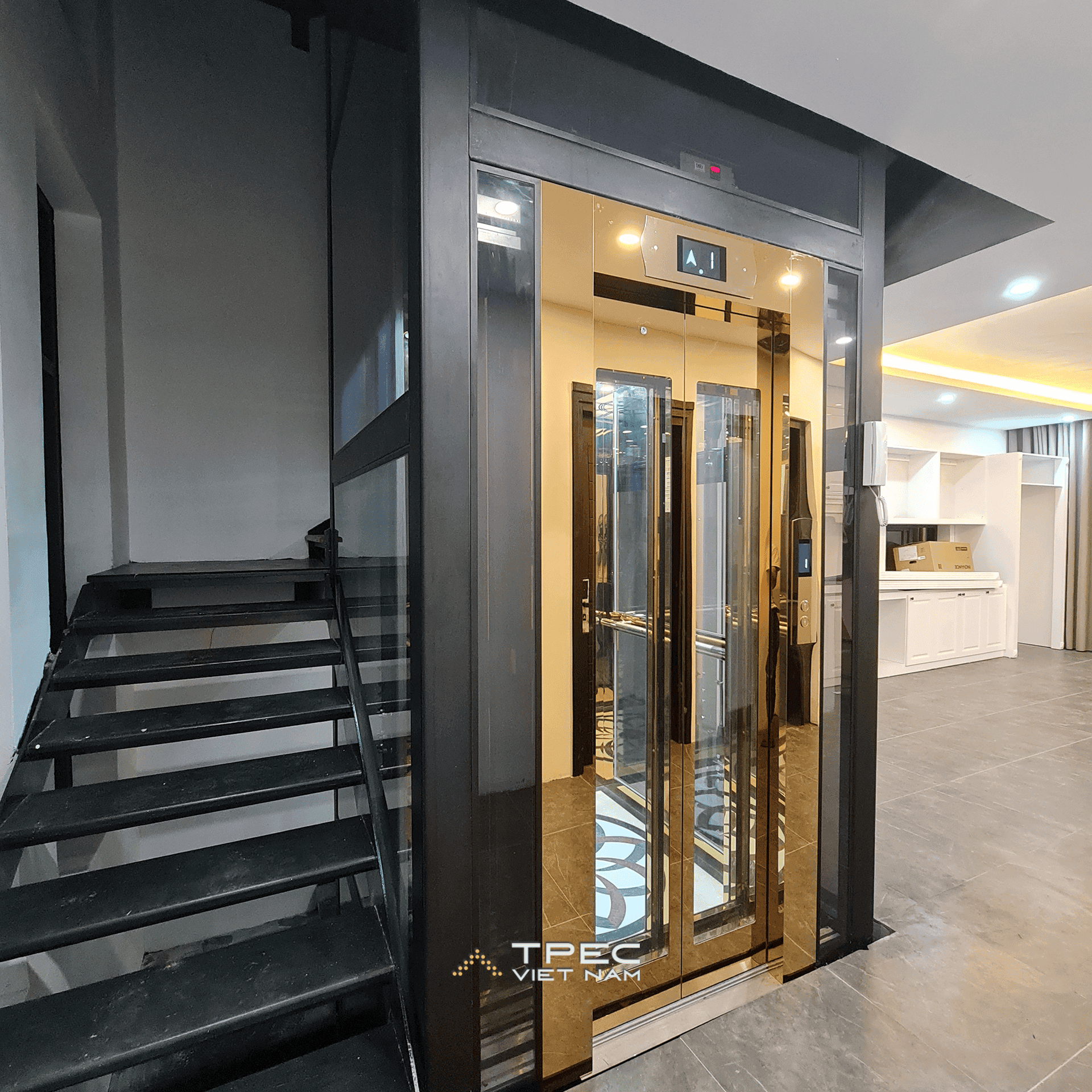 Giếng thang kính khung thép đen và cabin vàng thang máy 630kg bên cầu thang tại Sơn Tây