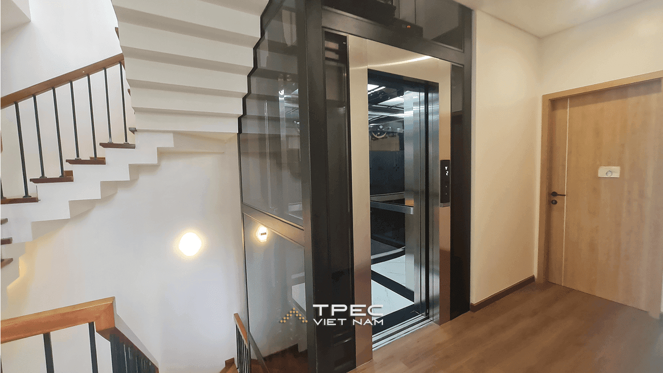 Giếng thang kính 630kg khung đen bên cầu thang trắng, cabin inox nhìn xuyên kính tại Đông Anh