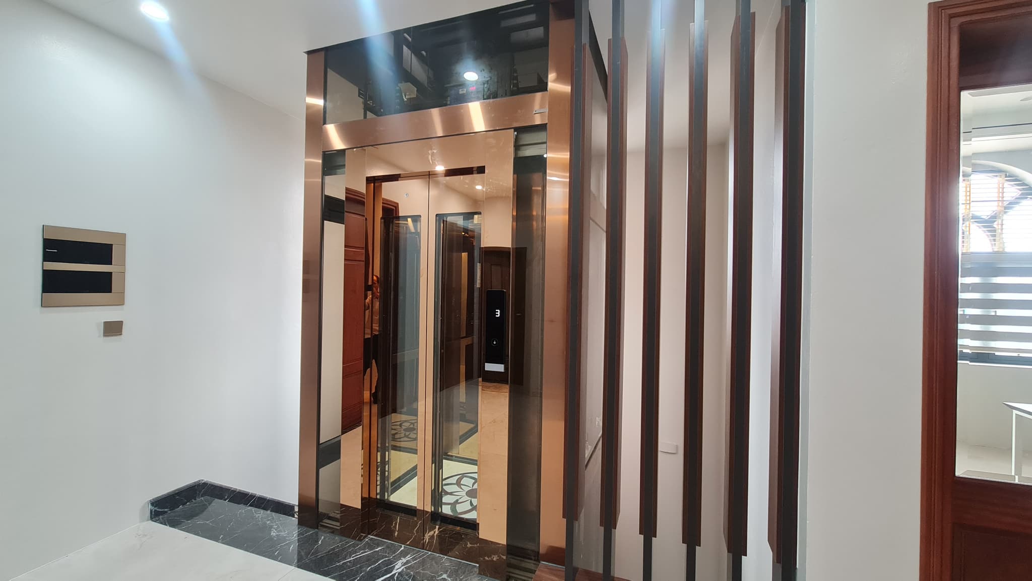 Cửa tầng thang máy kính 450kg khung inox gương ánh hồng, vách lam gỗ và ngưỡng cửa đá đen