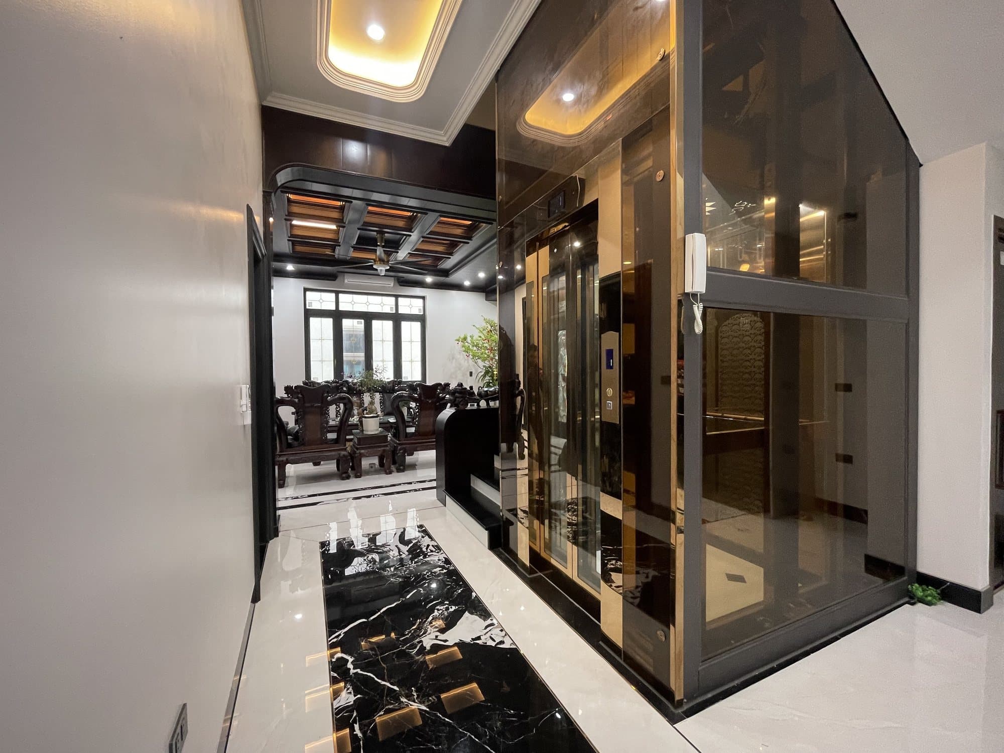Thang máy kính khung inox đồng, kính trà, trong phòng khách gỗ
